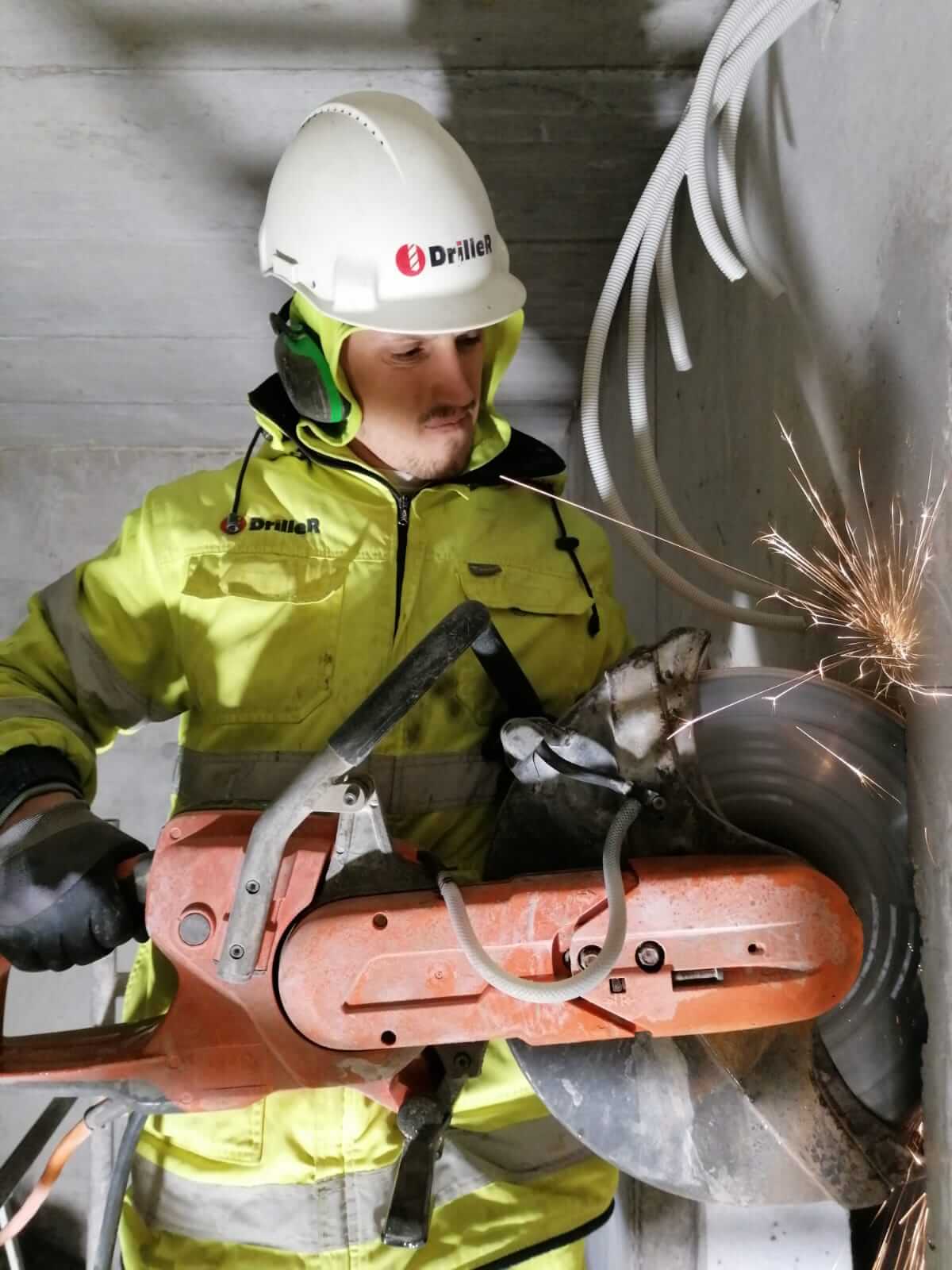 DrilleR meistars ar rokas zāģi prasmīgi zāģē betona sienu dzirkstelēm šķīstot 