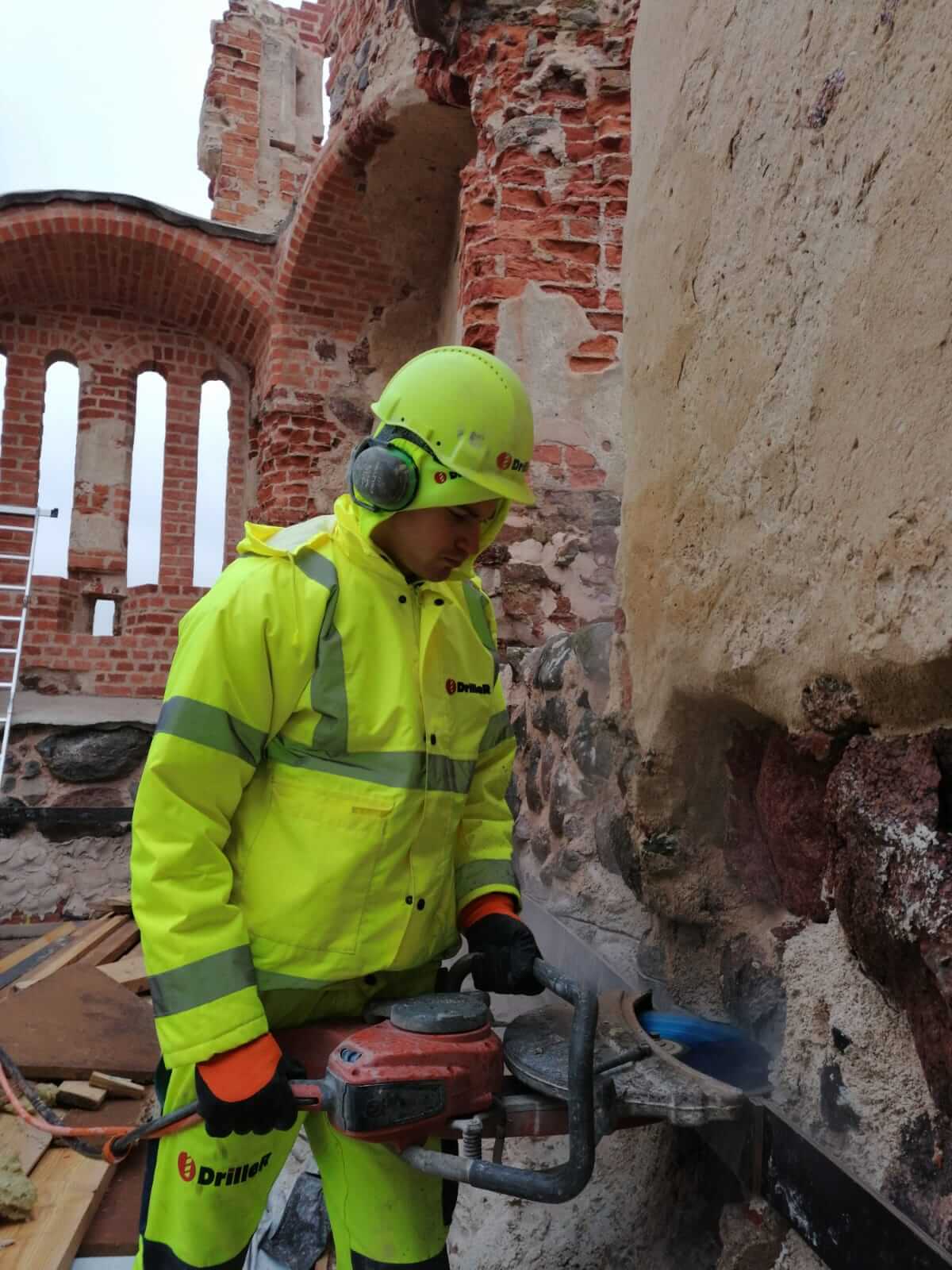 Driller meistars profesionāli veic senas laukakmeņu sienas zāģēšanu ar rokas zāģi
