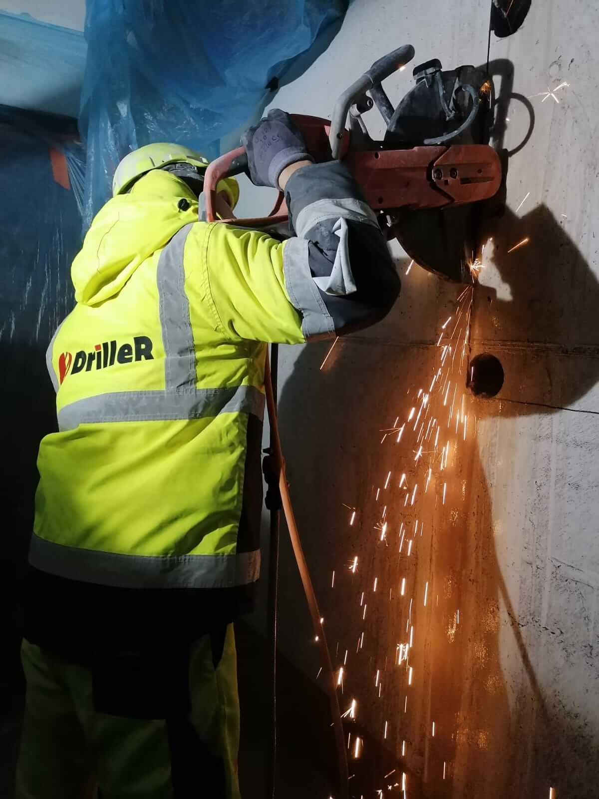 meistars zāģē ailu betona sienā kurā iepriekš izurbti caurumi stūros